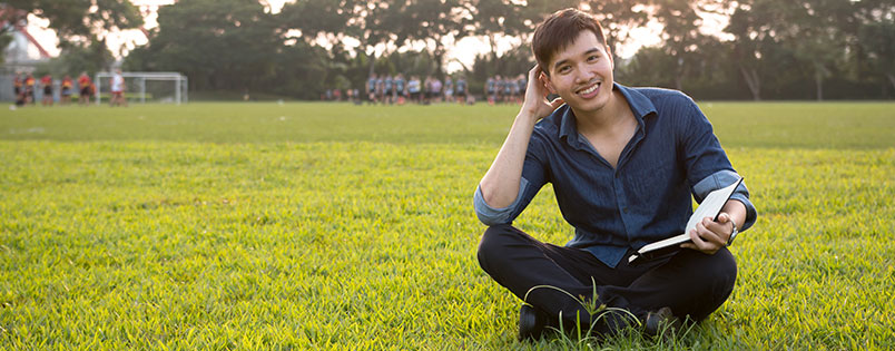 Happy student sitting in grass reading a book