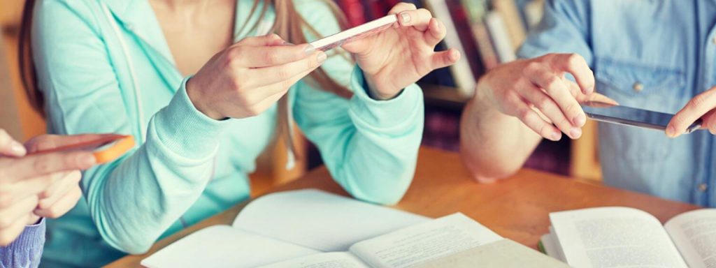 Students on their phones around a table with books