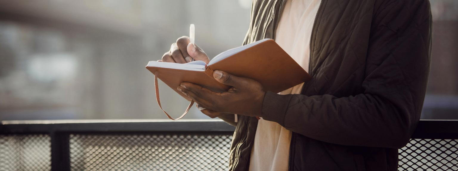 A man holding a notebook and writing in it